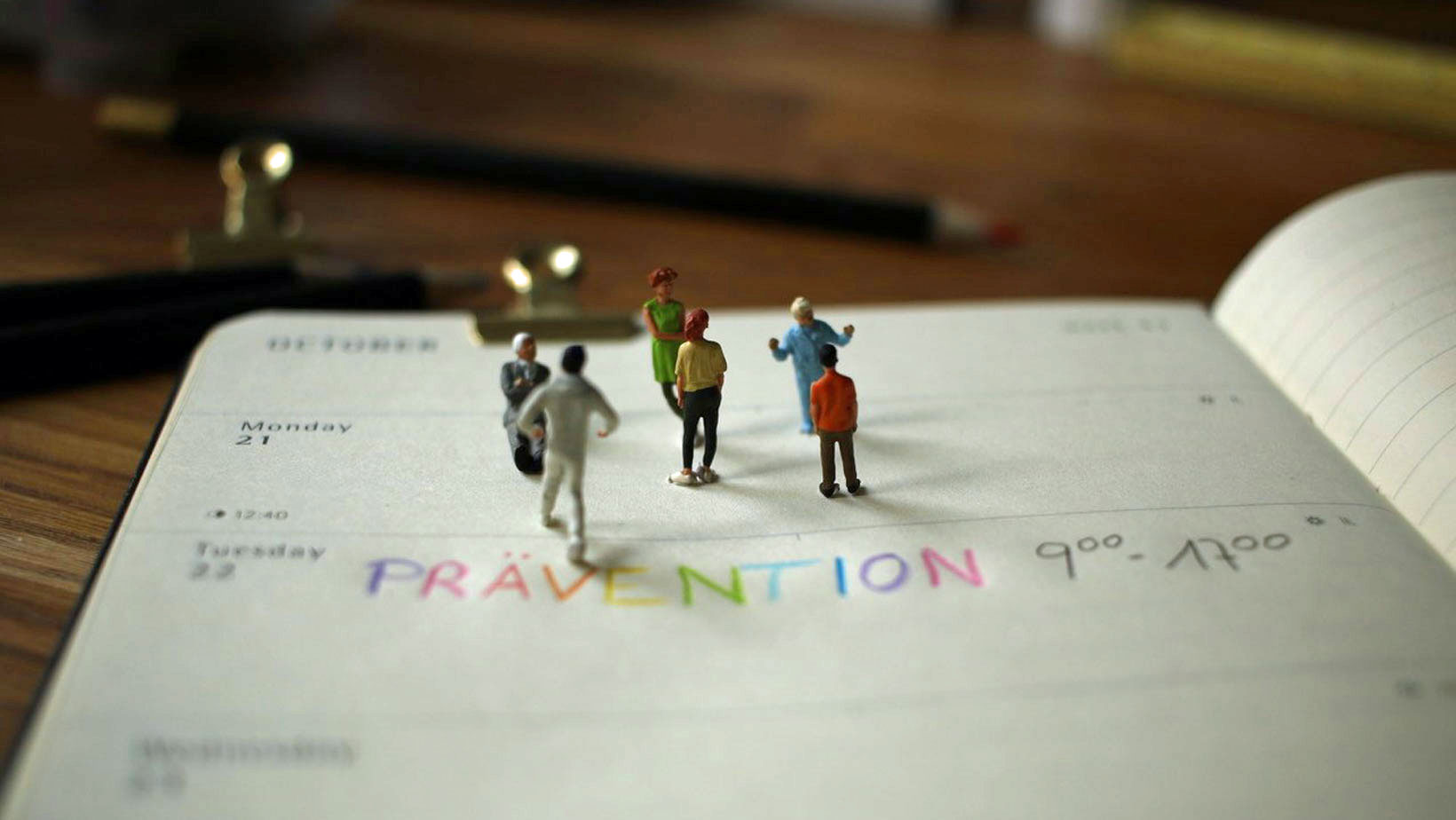 Modellfiguren stehen auf einem aufgeschlagenen Kalender, in dem ein Termin für eine Präventionsschulung eingetragen ist